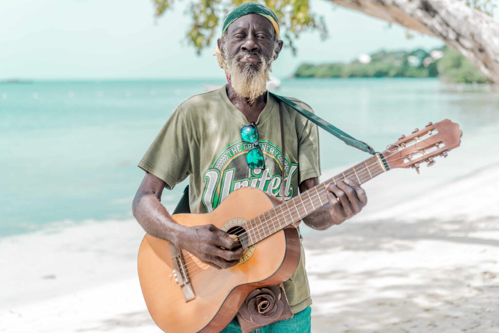 A Jamaican man plays the guitar on the beach in front of blue waters