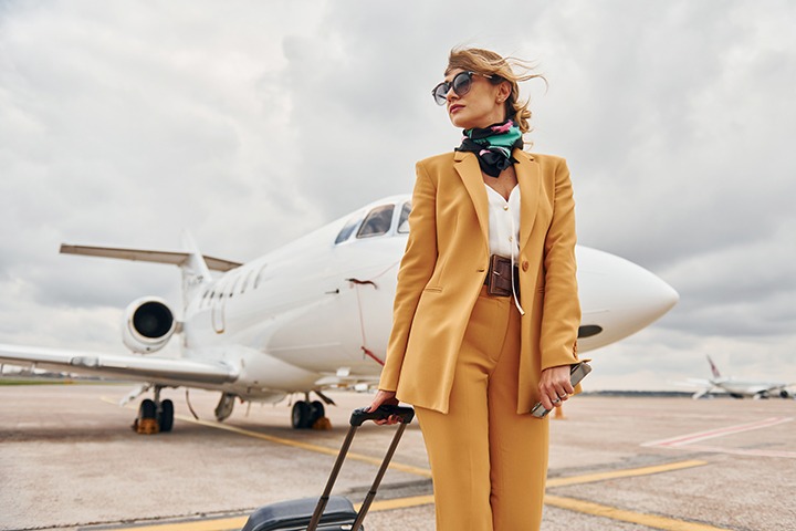 A glamorous woman in a yellow suit pulls a rolling suitcase behind her as she leaves a plane