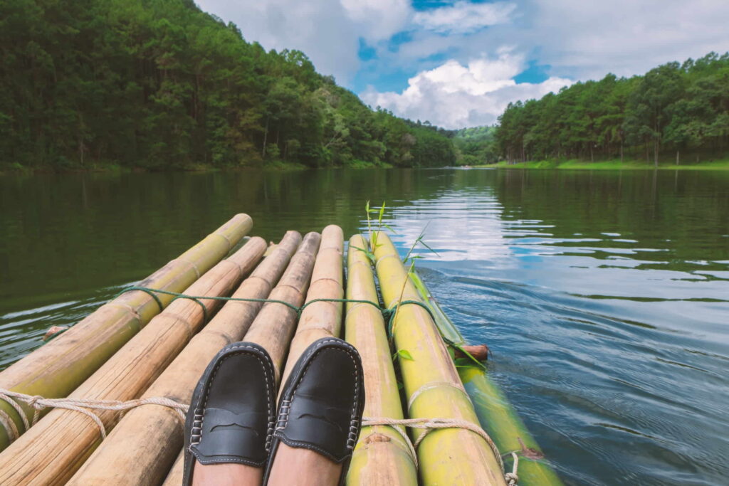 A point-of-view shot of someone sitting on a bamboo raft, looking out at the river