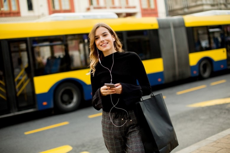 A woman stands in front of a bus, smiling